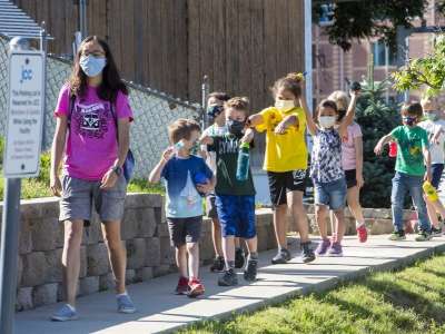 Kids in colorful shirts and masks walking single file